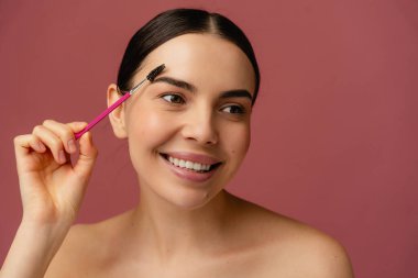 Pembe bir fırçayla çekici bir şahıs, kendine güvenerek gülümsüyor, canlı, pembe bir arka plana yaslanıyor, güzelliği ve kendine bakımı vurguluyor..