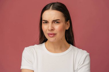 Kafası karışmış bir yüz ifadesi olan, sıradan giyinmiş, pastel pembe bir arka plana bakan birinin yakın çekimi. Kafa karışıklığı ve düşüncelere bağlı duygusal ve anlamlı içerik için mükemmel.