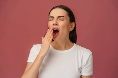 Sade pembe bir arka planla çevrili, açık bir esneme göstergesi, yorgunluğu vurguluyor.