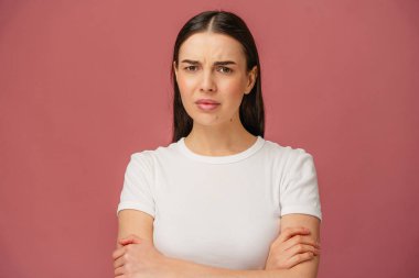 Resim, canlı pembe bir arkaplana karşı kollarını kavuşturan tuhaf bir ifadeye sahip bir insanı tasvir ediyor..