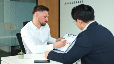 İki işadamı şirket büyümesini bir ofis toplantısında bir iş grafiğinde tartışıyor. Bir işadamı haritayı işaret ederek, Asyalı bir işadamına verileri açıklıyor.