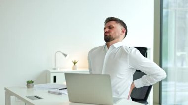 Ofiste çalışırken sırtı ağrıyan yorgun bir iş adamı. Masasında dizüstü bilgisayarla oturan beyaz gömlekli bitkin bir erkek..