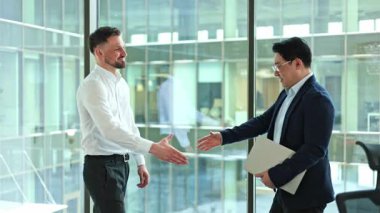 İki iş adamı, bir Asyalı, el sıkışıyor ve modern bir ofisin penceresinin yanında bir şey tartışıyorlar. İkisi de mutlu..