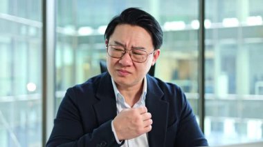 Stresli Koreli iş adamının modern bir ofiste boğazı ağrır. Mutsuz erkek yönetici öksürüyor ve yutkunmakta zorlanıyor..