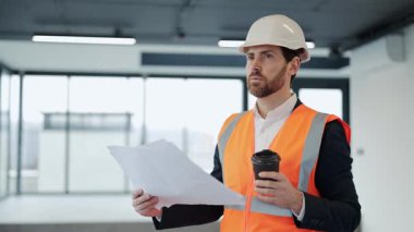 Başarılı mimar planları gözden geçirir ve ofiste kahve içer. Resmî giysili ve şapkalı profesyonel iş adamı boş bir alanda duruyor. Düşünceli ve kendinden emin..