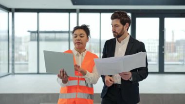 Profesyonel mühendis ve yatırımcı modern ofiste inşaat planlarını tartıştılar. Yatırımcı planları elinde tutuyor, mühendis dizüstü bilgisayar kullanıyor. Ekip çalışması ve inşaat alanında uzmanlık.