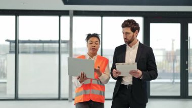 Kadın Afrikalı Amerikalı profesyonel mimar ve mühendis modern bir ofiste bina planlarını tartışıyor. Odaklanmış, işbirlikçi ve kendinden emin hissediyorlar. Ticari gayrimenkul yatırımlarında uluslararası işbirliği anlaşması