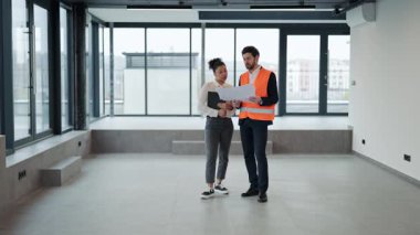 Başarılı yatırımcı ve profesyonel mimar boş ofiste planları tartışıyor. İş ortakları yenilemeyi planlıyor ve yeni çalışma alanı için heyecanlı.