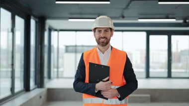 Resmi giysili başarılı mühendisin portresi, güvenlik yeleği pano tutuyor, gülümsüyor ve modern ofis binasında mutlu hissediyor. Uluslararası anlaşma emlak yatırımı.