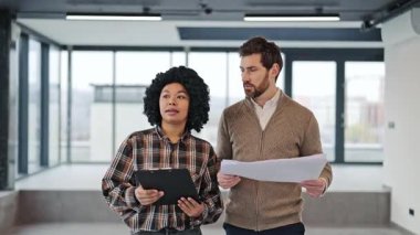 Profesyonel meslektaşlar modern boş ofis alanının mimari planlarını tartışırlar. İş ortakları şık ofis kıyafetleriyle yeni bir proje planlıyor.