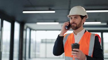 Başarılı bir mimar telefonda konuşuyor ve kahve içiyor. İnşaat alanında çalışan resmi giysili ve şapkalı profesyonel bir işadamı. Modern bina.