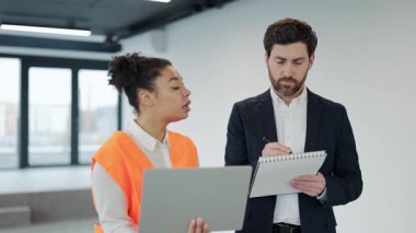 Profesyonel mühendis ve iş adamı kapalı alanda bir projeyi tartışıyor. Yatırımcı notlar alırken uzmanlar ona bir dizüstü bilgisayardan bilgi veriyor. Başarılı takım çalışması.