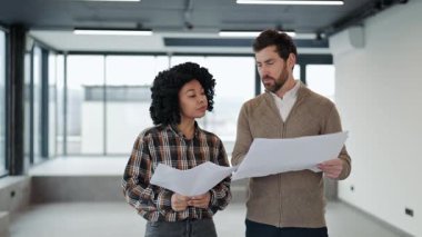 Profesyonel meslektaşlar modern boş bir ofis alanının planlarını tartışırlar. Uzmanlar planlarını gözden geçirirler, günlük giysiler giyerler, ortak bir projede..