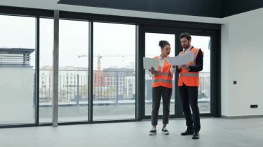 Ticari gayrimenkul yatırımlarında uluslararası işbirliği anlaşması başarılı iş adamı ve güvenlik yelekleri giyen iş kadını planları ve bir dizüstü bilgisayarı tartıştılar. İnşaat alanı, takım çalışması ve uzmanlık.