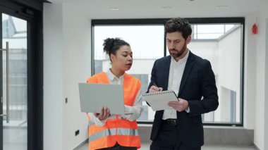 Profesyonel mimar ve inşaat mühendisi modern bir ofiste inşaat planlarını tartışıyor. Odaklanmış ve kararlı hissediyorlar..