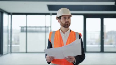 Resmi takım elbiseli düşünceli bir mimar ve boş modern ofisin planlarını gözden geçiriyor. Proje detaylarını analiz eder, geliştirme stratejisini planlar. Odaklanma, konsantrasyon ve profesyonellik.