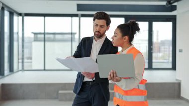 Başarılı iş adamı ve kadın mühendis modern ofiste planları tartışıyor. Takım elbiseli profesyonel mimar ve güvenlik yeleği uzmanı proje üzerinde işbirliği yapıyor..