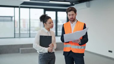 Profesyonel mimar ve yatırımcı boş bir ofiste planları tartışıyor. Gelecekteki çalışma alanı tasarımını planlarken odaklanmış hissediyorlar..