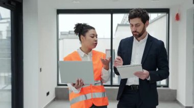 Yakışıklı profesyonel yatırımcı ve inşaat mühendisi modern bir binada bir projeyi tartışıyorlar. Resmi olarak giyinmişler ve bir iş toplantısında kendilerini güvende ve odaklanmış hissediyorlar..