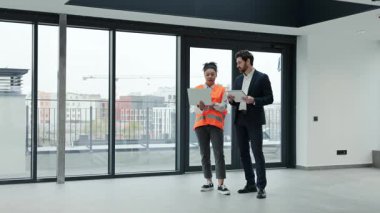 Profesyonel yatırımcı ve mimar modern ofis alanındaki inşaat planlarını tartışıyor. Coşkulu ve odaklanmış hissediyorlar. Ticari gayrimenkul yatırımlarında uluslararası işbirliği anlaşması