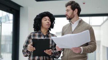 Profesyonel meslektaşlar modern bir ofiste bir projeyi tartışıyorlar. Bir iş kadını ve işadamı şık giyinir ve dokümanları inceler..