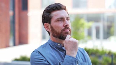 Düşünceli gündelik giysiler içinde bir iş adamı dışarıda dikiliyor ve şirketinin geleceğini düşünüyor. Erkek kendini ilham almış ve mutlu hisseder..