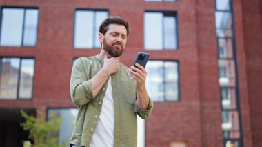 Hüsrana uğramış adamın boğazı ağrıyor, dışarıda kendini kötü hissediyor. Gündelik tişört giyen şık bir adam akıllı telefon kullanır, üzücü haberler verir, üzüntüsünü dile getirir..