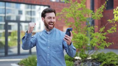 Heyecanlı iş adamı günlük giysiler içinde dışarıda neşe, başarı ve mutluluğu ifade ediyor. Profesyonel adam zaferi kutluyor, modern binanın yakınında mutlu ve neşeli hissediyor..