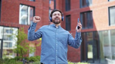 Günlük kıyafetlerle dans eden ve dışarıda, tuğla binanın yanında kulaklıkla müzik dinleyen yakışıklı bir adam. Mutlu, neşeli, kaygısız hissediyor..