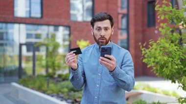 Kredi kartı ile hayal kırıklığına uğramış işadamı akıllı telefondan online alışveriş yapmada sorun yaşıyor. Mavi gömlekli şık adam dışarıda negatif duygular yaşıyor..