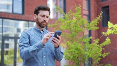 Açık havada akıllı telefon kullanan, hayal kırıklığına uğramış iş adamı. Yakışıklı bir adam ofis binası yakınlarında kötü haber okurken kafası karışık ve rahatsız..