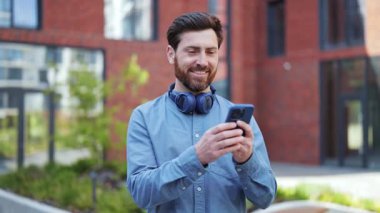 Smartphone 'u ofis binasının yakınında kullanırken mutlu iş adamları. Profesyonel uzman modern ofis binasının yanında dururken kendini mutlu hissediyor.