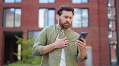 Hasta adamın portresi telefonunda kötü haber okurken göğsünde ağrı hisseder. O dışarıda duruyor ve günlük giysiler giyiyor. Kalp krizi, sağlık sorunu. Solunum zorluğu, sağlık sorunları konsepti.