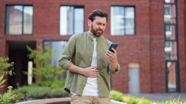 Hasta adam bir apartmanın yakınında telefon kullanırken mide ağrısı hisseder. Erkek serbest giyiniyor ve hayal kırıklığına uğramış ve iyi hissetmiyor..