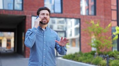 Günlük giysiler içinde yakışıklı bir iş adamı dışarıda hoş bir telefon konuşması yapıyor. Başarılı bir adam kentte konuşurken mutlu olur ve gülümser..