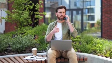 Odaklanmış iş adamı uzaktan çalışır. Telefonda konuşan ve dışarıda dizüstü bilgisayar kullanan başarılı bir adam. Günümüz ofis çalışanı günlük giysiler içinde bankta oturuyor..