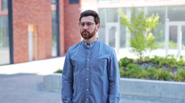 Gözlüklü ve kollarını kavuşturup kameraya gülümseyen rahat gömlekli yakışıklı bir iş adamı. İş bölgesi. Başarılı uzman kendinden emin..