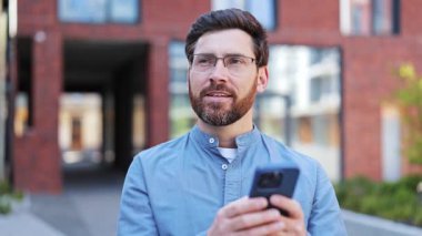 Bir ofis binasının yanında akıllı telefon kullanan mutlu yakışıklı bir işadamı. Gülümser ve bir mesaj okurken mutlu hisseder..