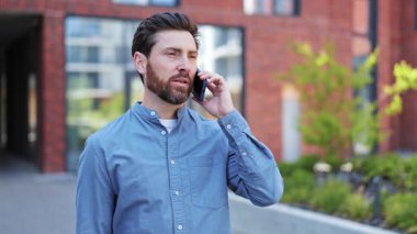 Akıllı telefondan konuşan yakışıklı bir iş adamı. Ofis bölgesinde cep telefonu kullanan rahat gömlekli başarılı bir adam. Mutlu girişimci iyi duygular hisseder.