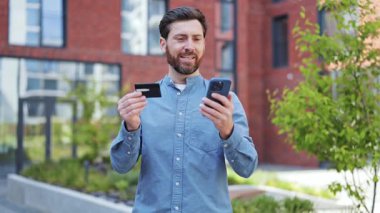Akıllı telefondan alışveriş yapan mutlu yakışıklı adam. Başarılı iş adamı çevrimiçi ödeme için cep telefonu ve kredi kartı kullanıyor. Smartphone Kredi Kartıyla Çevrimiçi Ödeme Yapan İşadamı
