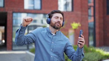 Gündelik giysiler içindeki olumlu adam, şehirdeki kablosuz kulaklıklarla müzik dinlemekten hoşlanıyor. Erkek mutluluğu, mutluluğu ve özgürlüğü hisseder..