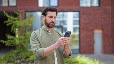 Ofis binası yakınlarında günlük kıyafetleriyle hayal kırıklığına uğramış iş adamı akıllı telefon kullanırken diş ağrısı çekiyor. Acı, stres ve hoşnutsuzluk hissediyor..