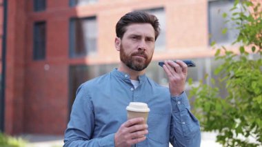 Günlük giysiler içinde yakışıklı bir iş adamı elinde kahve ve açık havada akıllı telefon kullanıyor. İş, iş, iletişim konsepti.