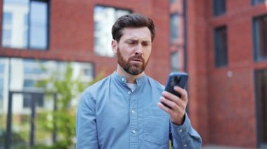 Hüsrana uğramış iş adamı bir tuğla binanın önünde oturup telefonuna bakarken stresli hissediyor. Sinirli İşadamı, telefonundaki kötü haberden ötürü stresli