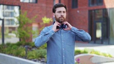 Günlük giysiler içinde yakışıklı bir iş adamı dışarıda kulaklık takıyor. Profesyonel adam ofis yakınında müzik dinlemeyi sever. Mutlu, neşeli ruh hali.