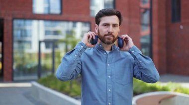 Günlük giysiler içinde yakışıklı bir iş adamı kulaklıkla dışarıda müzik dinliyor. Başarılı bir serbest yazar ofis yakınında müzik dinler. Olumlu duygular, başarı, mutluluk.