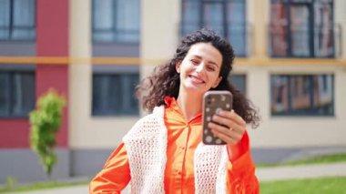 Dışarıda başarıyı kutlayan heyecanlı kadın. Turuncu ve beyaz giysili şık bir kadın, evinin yanında mutlu ve neşeli hissediyor..