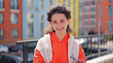 Günlük giysiler içindeki neşeli esmer kadın portresi şehir binalarının arka planındaki kameraya gülümsüyor. Mutlu ve mutlu hissediyor..