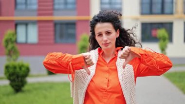 Parlak kıyafetler giymiş şık bir kadın dışarıda dikilirken baş parmağını kaldırıyor. Hoşnutsuzluk, olumsuz geri bildirim ve onaylamama konsepti..