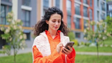 Dairenin yakınında telefon kullanan neşeli bir kadın. Turuncu gömlek ve örgü yelek giyiyor..
